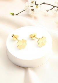 Orecchini a perno a forma di fiore in oro con superficie testurizzata, montati su una base circolare bianca. Design semplice ed elegante.