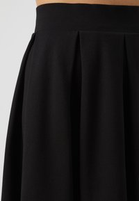 Gonna nera plissettata con una texture liscia e una vita elastica. Il tessuto appare morbido e si drappeggia in modo elegante.