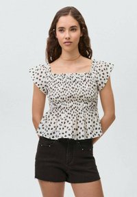 Blusa bianca con stampa floreale nera, corpino arricciato e maniche a volants, abbinata a pantaloni corti in denim neri. Tessuto liscio, design casual.