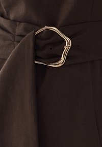 Tmavohnedý textilný opasok so skrútenou zlatou metalickou prackou pripevnený okolo látky zodpovedajúcej oblečenia.