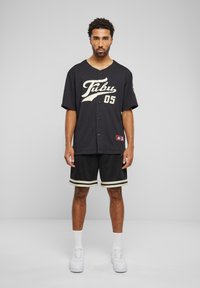 Jersey de baseball negru, cu litere și butoane albe, asociat cu pantaloni scurți din plasă negri, cu dungi albe și aurii. Adidași albi.
