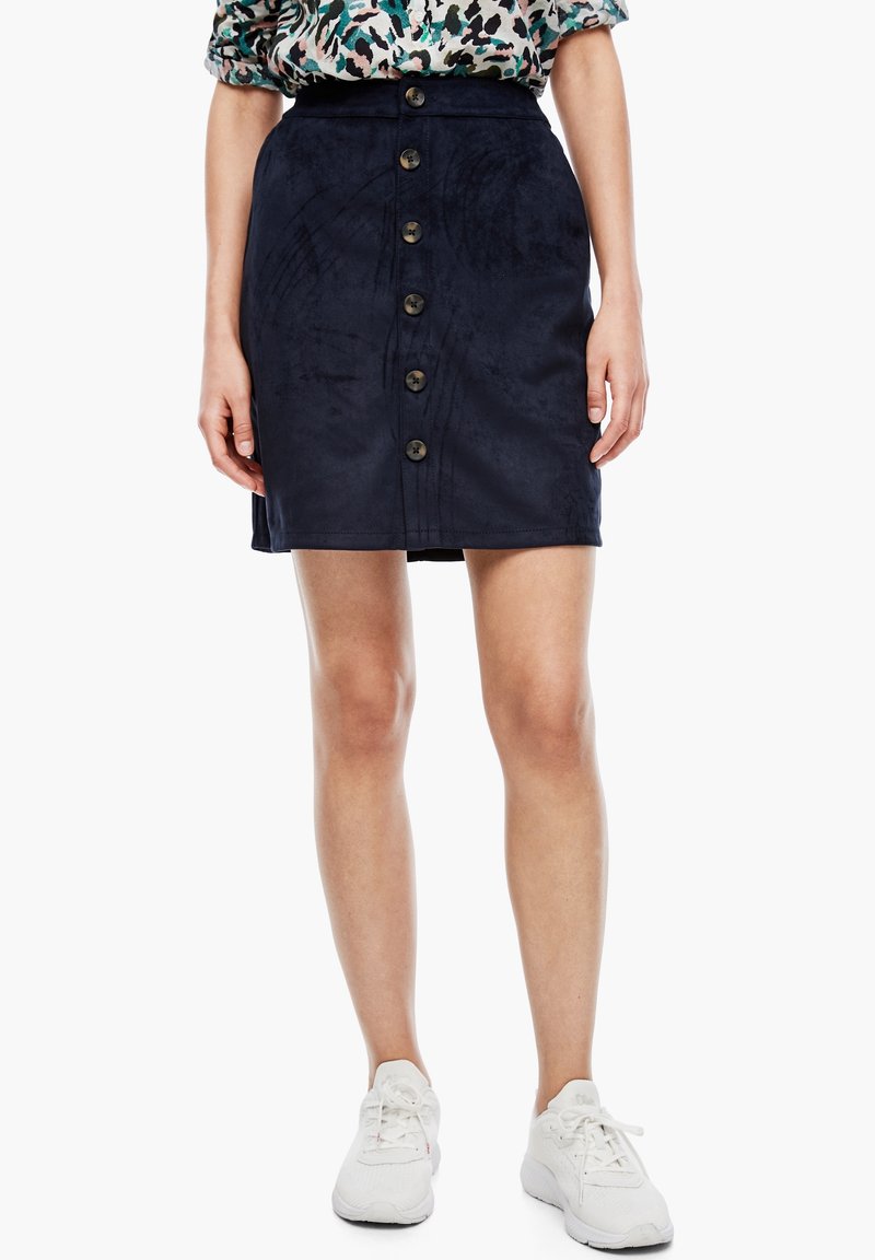 Minifalda de ante azul oscuro con corte recto, que presenta un cierre frontal con botones y detalles texturizados. Se lleva con zapatillas deportivas blancas.