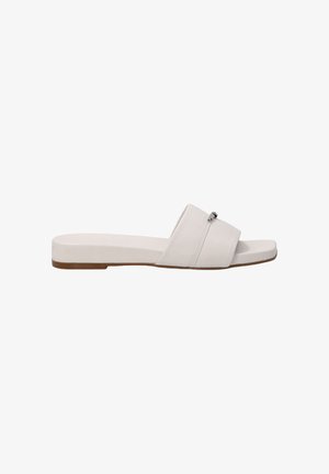 White flat sandals with cross straps, made of textured material. Features a minimalistic design and a low heel with a tan sole.