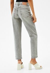 Jeans alti grigi con vestibilità rilassata, dotati di un logo cucito sul retro, dettagli cuciti e orlo sfilacciato. Abbinati a tacchi a blocco bianchi.