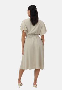 Vestido beige a la altura de las rodillas con mangas cortas y rizadas, cintura fruncida y falda fluida. Tela suave y ligera con una textura sutil.