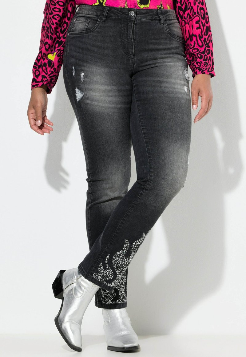 Jeans de mezclilla negra con detalles desgastados y un patrón de llamas acentuado con rhinestones en el dobladillo. Diseño ajustado, forma de pierna entallada.