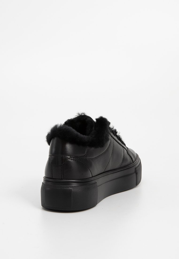 Czarne skórzane sneakersy z pluszowym czarnym futrem wzdłuż kołnierza, płaską gumową podeszwą, pikowanym wzorem i teksturowanym gripem na podeszwie.