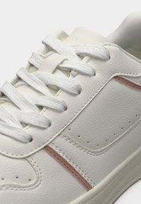 Κοντινό πλάνο λευκού δερμάτινου αθλητικού παπουτσιού με λευκά κορδόνια και διακριτική ροζ ρίγα κατά μήκος της πλευράς.