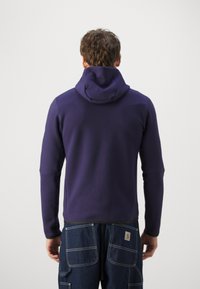 Sweat à capuche violet à manches longues, design ajusté et texture douce. Associé à un pantalon en denim bleu avec plusieurs poches.