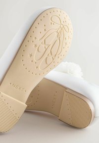 White fabric shoe sole with a textured light tan base, featuring ballet slipper design and star patterns, branded "NEXT."