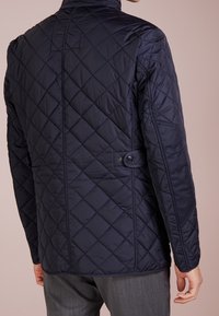 Navy pikowana kurtka z kołnierzem stójkowym, bocznymi guzikami i gładką fakturą. Posiada dopasowany krój oraz detale w szwach.