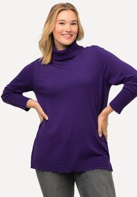 Maglione a collo alto viola con maniche lunghe, dettagli a coste sui polsini e vestibilità rilassata; abbinato a pantaloni grigi. Texture morbida e lavorata a maglia.
