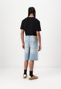 T-shirt noir à manches courtes, short en denim bleu clair et baskets beiges avec des accents de talon blancs. Tissu lisse, coupe décontractée et design mi-long.