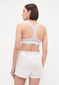 Calvin Klein sportmelltartó világosszürkében, mintás textúrával és versenyhátsó kialakítással. Fehér rövidnadrággal párosítva, rugalmas derékpánttal.
