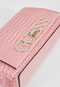 Rosa falsk læder clutch med krokodilletekstur, der har en guldlåseklap på forsiden. Fyrkantet form med en glat overflade og kontrasterende kanter.