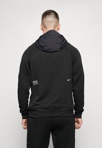 Czarna bluza z kapturem z fakturowanej tkaniny z oddychającą siateczką, logo Nike oraz metką po lewej stronie na dole.