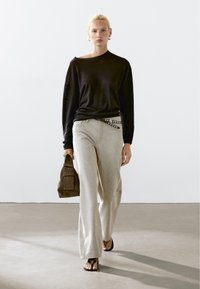 Zwarte lange mouwen shirt, lichtgrijze wijde broek met een zijriem met metallic accenten, en een donkerbruine tas. Eenvoudig schoeisel.