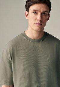 Olivengrøn kortærmet t-shirt med rund halsudskæring, lavet af blødt, tekstureret stof, med en afslappet pasform og enkelt design.