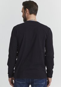 Hosszú ujjú fekete póló, 100% pamutból készült, kerek nyakkivágással és sima felülettel, hátulról látható, kék farmernadrággal párosítva.