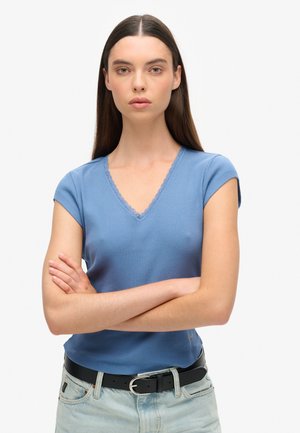 Lichtblauw geribbeld V-hals T-shirt met korte mouwen. Bevat een delicate kantafwerking rond de halslijn. Draagt bij hoge taille jeans en een zwarte riem.
