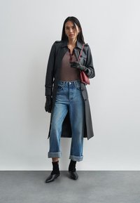 Czarny długi płaszcz na brązowym prążkowanym topie, niebieskie podwinięte dżinsy, czarne rękawiczki i czarne botki na obcasie, dopełnione czerwonym torebką.