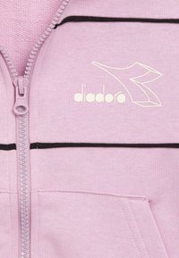 Felpa con cappuccio rosa chiaro con zip, dettagli a strisce nere e logo bianco stampato. Realizzata in tessuto morbido con una texture liscia.