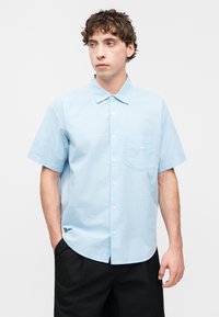 Πουκάμισο με κοντά μανίκια σε ανοιχτό γαλάζιο βαμβάκι, με τσέπη στο στήθος που φέρει λευκό λογότυπο και κλασικό γιακά.