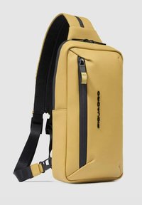 Zaino giallo dal design elegante, realizzato in materiale liscio. Presenta una tasca nera con cerniera, tracolla regolabile e accenti minimalisti.