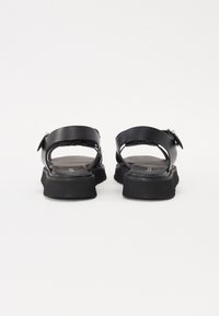 Sandale negre cu curele din piele netedă, talpă groasă din cauciuc și cataramă reglabilă. Designul este deschis, cu un toc plat pentru stabilitate.