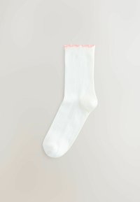 Biała prążkowana skarpetka do kostki z ozdobnym, różowym falbankowym wykończeniem u góry. Gładka tekstura, dopasowany kształt, bez widocznych znaków firmowych ani wzorów.