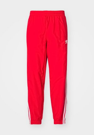Red athletic pants with an elastic waistband, white striped accents along the sides, and a small white logo on the left thigh.