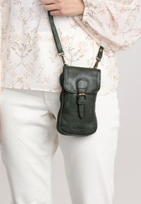 Green leather crossbody bag with a flap closure, zipper, and buckle detail. Shiny finish, compact design, and adjustable strap.