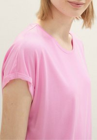 Rosa kortärmad topp med rund halsringning, utrustad med rullade ärmslut och en mjuk, slät textur.