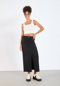 Black denim maxi skirt with a front slit, paired with a white ribbed crop top. Model wears chunky white platform sandals.