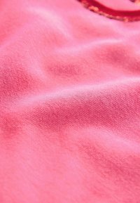 Tissu rose doux avec une texture fine en tricot et des plis subtils, montrant une partie d'un détail floral arrondi dans le coin supérieur droit.