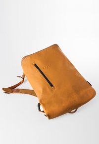 Sac à dos rectangulaire en cuir marron clair avec poche zippée verticale noire à l'avant et bretelles rembourrées réglables sur fond blanc.