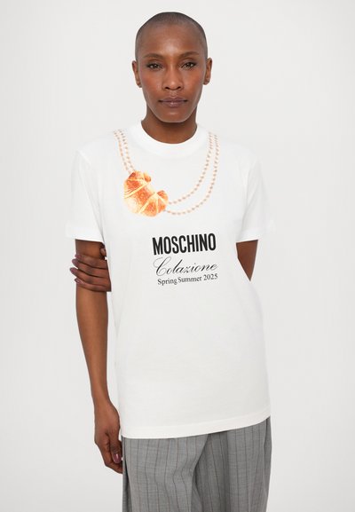 White cotton t-shirt featuring a croissant graphic and pearl necklace design. Black lettering reads "Moschino Colazione Spring Summer 2025."