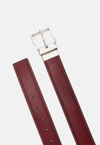 Ciemnoczerwony skórzany pasek z podwójną klamrą w kolorze srebrnym i przeszytymi krawędziami na białym tle.