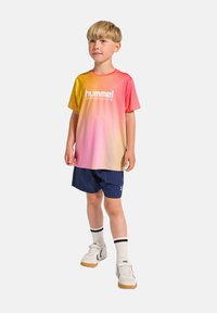 Kortärmad tröja med gradient som övergår från gult till rosa, med "hummel PERFORMANCE"-logotyp, i kombination med marinblå shorts och vita sneakers.