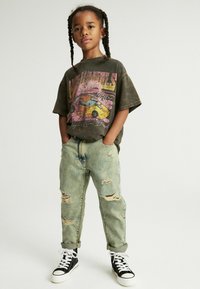 Camiseta gráfica de color gris oscuro con un diseño de coche vibrante, combinada con unos jeans claros desgastados y zapatillas altas negras.