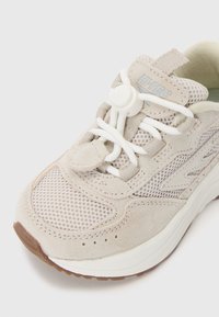 Lys grå sneaker med mesh- og suede-materialer, rund tå, hvite snører, elastisk snørelås og teksturert gummisåle.