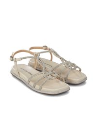 Sandalias planas beiges con correas plateadas brillantes, que presentan un diseño anudado y una suela acolchada y texturizada para mayor comodidad.