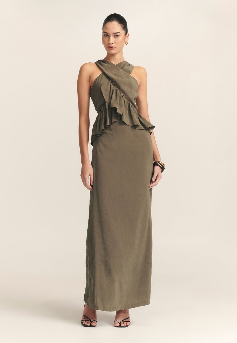 Olijfgroene maxi-jurk met een gerimpelde, asymmetrische lijfje en gekruiste bandjes. Draag met zwarte sandalen met bandjes, die een gladde textuur tonen.