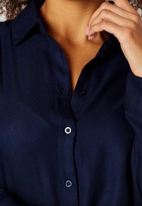 Camicia blu navy con tessuto morbido. Presenta un colletto, bottoni frontali e una vestibilità comoda.