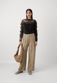 Top nero trasparente con maniche a volant, abbinato a pantaloni di lino beige a vita alta e borsa beige testurizzata. Scarpe beige intrecciate completano l'outfit.