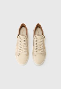Beige lærersneakers med en teksturert tan-accent ved hælen, glatt overflate og elastiske snøringer; har en sideglidelås for enkel påkledning.