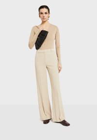 Bež majica s dugim rukavima, kremaste hlače širokih nogavica i teksturirana crna torba na preklop. Smuštare smešnih boja upotpunjuju izgled. Jednostavan, moderan dizajn.