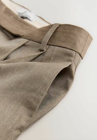 Hnědé kalhoty z texturované tkaniny s plochým předním dílem, viditelným šitím a klasickým designem pasu. Obsahují jemný vzor proužků.
