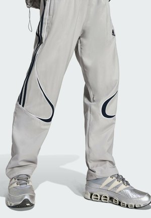 Pantalon de sport gris clair avec des accents bleu foncé et des détails en passepoil, assorti à des baskets argentées avec une finition texturée et un design unique de semelle.