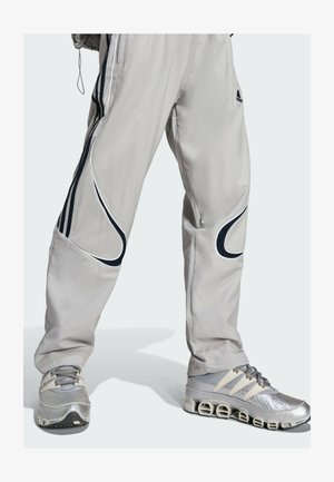 Pantalon de sport gris clair avec des accents bleu foncé et des détails en passepoil, assorti à des baskets argentées avec une finition texturée et un design unique de semelle.